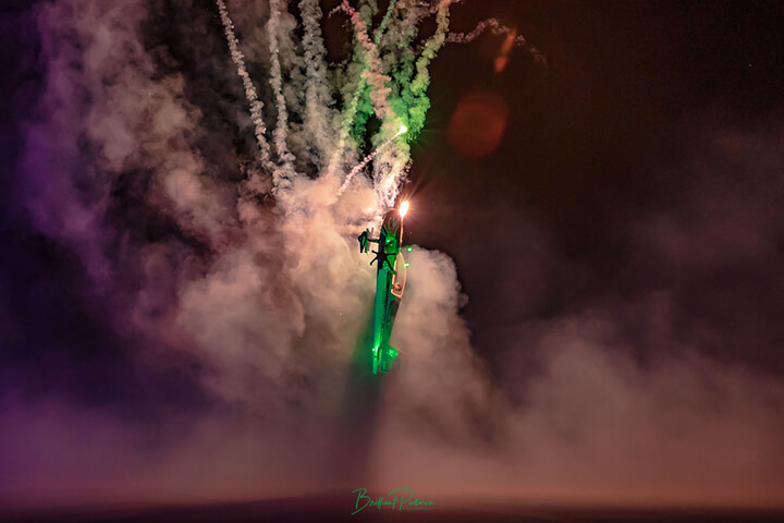 A low-wing rc aerobatic plane vertically climbs into a fireworks display.